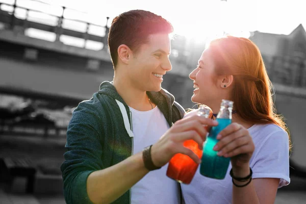 Cheerful couple clanging their bottles while drinking lemonade — Stock Photo, Image