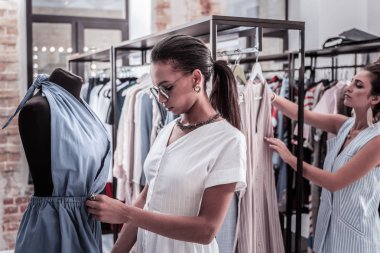 Yeni koleksiyonundan giysiler asılı butik çalışan iki yardımcıları