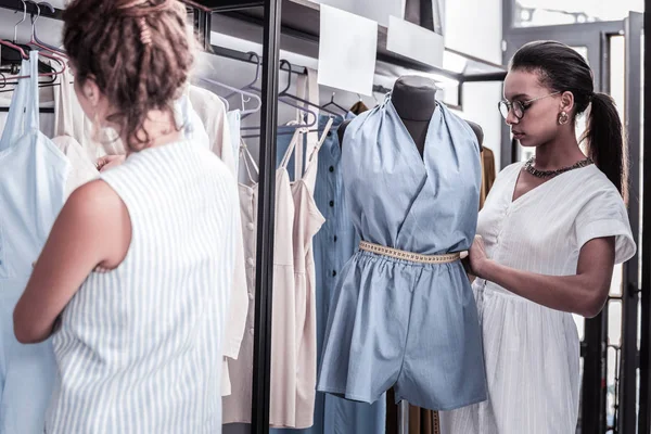 Workers of fashion boutique putting clothes from new collection on hangers