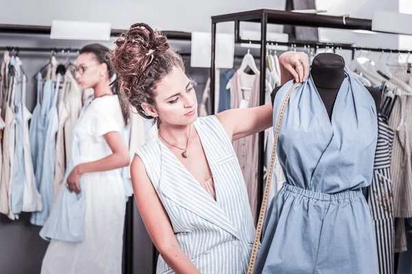 Fashion designer with hair bun standing near body form with tape measure