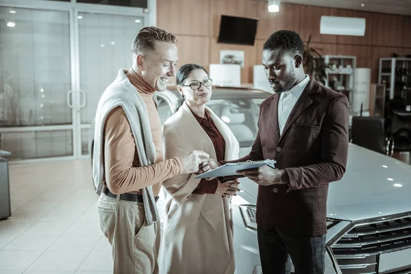 Glada affärsman klädd i orange sköldpadda hals underteckna dokument — Stockfoto