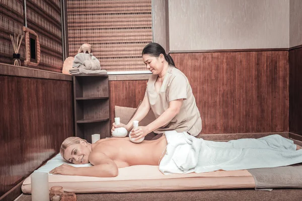 Gioioso abile massaggiatrice facendo massaggio con borse speciali — Foto Stock