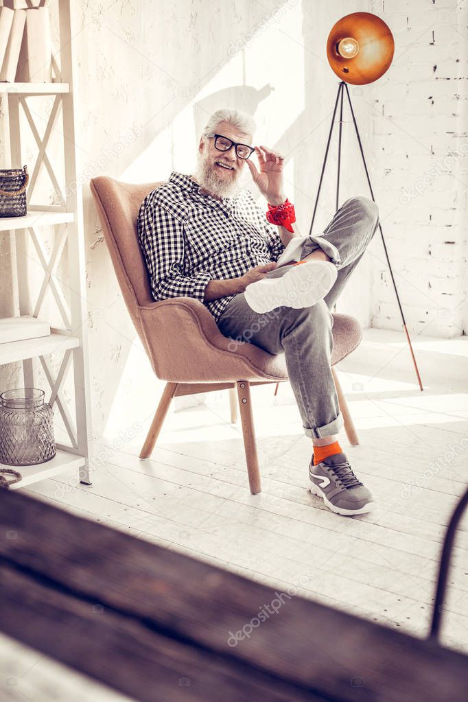 Pleased bearded man sitting in stylish armchair