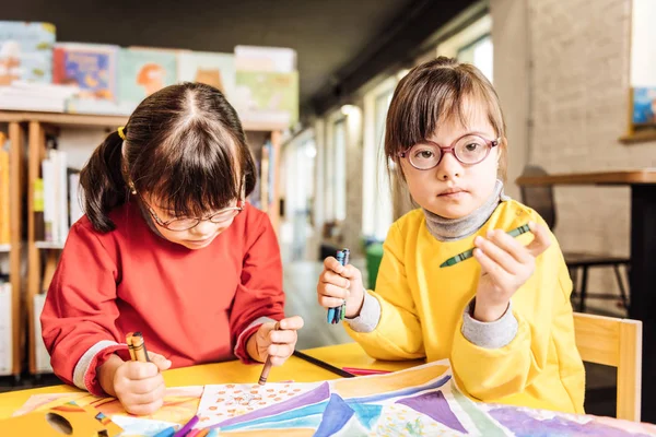 Dark-eyed sisters with Down syndrome coloring pictures together — Stock Photo, Image