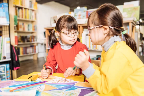 Sisters with Down syndrome coloring pictures in kids library — Stock Photo, Image