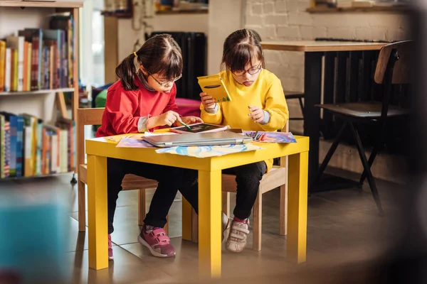Дві дівчини дошкільного віку з синдромом Дауна тримають барвисті олівці — стокове фото