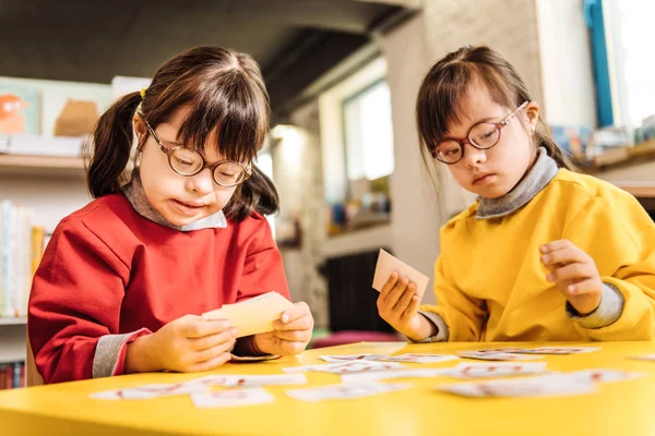 Gemelos de ojos oscuros con trastorno genético sentados a la mesa y jugando — Foto de Stock