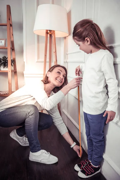 Angenehme nette Frau, die ihre Töchter in der Größe misst — Stockfoto