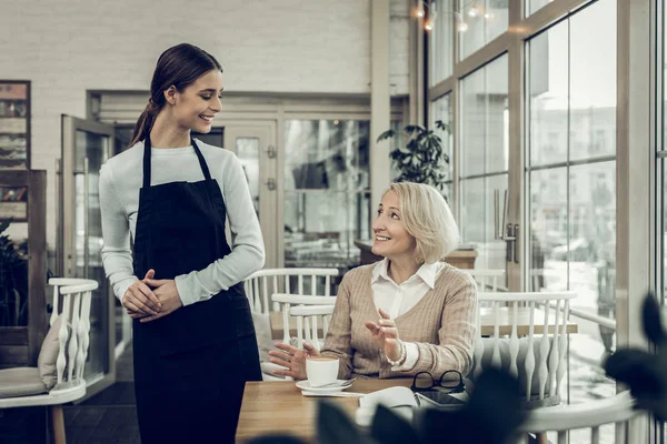 Усміхнена приємна офіціантка говорить зі своїм постійним клієнтом — стокове фото