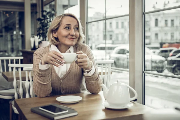 Agradable mujer madura sintiéndose bien mientras bebe té en la cafetería — Foto de Stock