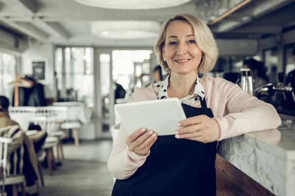 Blonde-haired entrepreneur owing restaurant holding little white tablet
