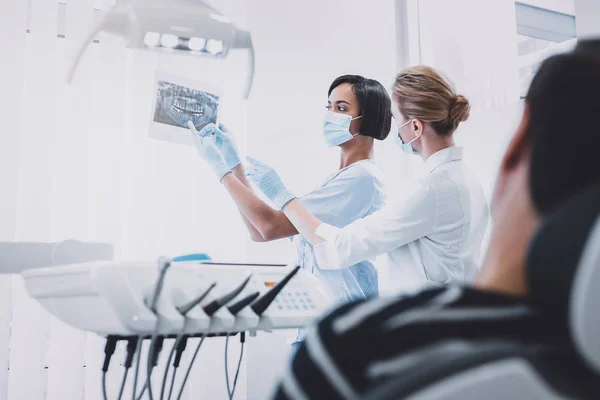 Dentista internacional competente consultando seu jovem assistente — Fotografia de Stock