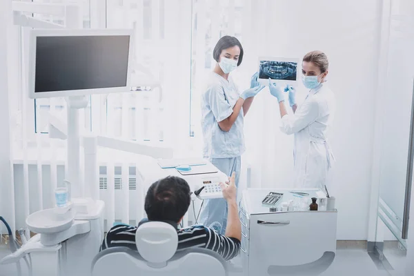 Vrolijke jonge internationale tandarts demonstreren röntgen foto — Stockfoto