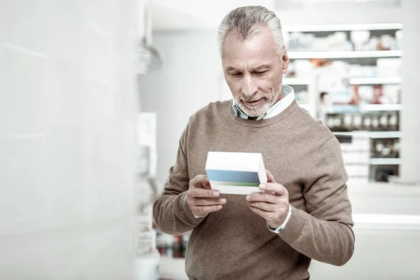 Бородатый мужчина читает содержимое таблеток, покупая лекарства для своей жены — стоковое фото