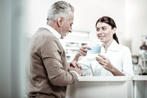 Pleasant cheerful dark-haired pharmacist talking to her grey-haired client — Stock Photo, Image
