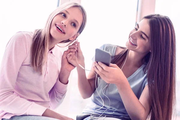 Smiling girl giving to her friend headphones — Stock Photo, Image