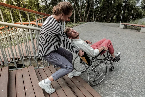 Amable chica ayudando a levantar silla de ruedas con inválido — Foto de Stock