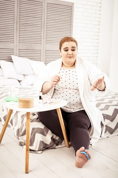 Mujer pelirroja con sobrepeso revisando su manicura mientras está sentada en la cama — Foto de Stock