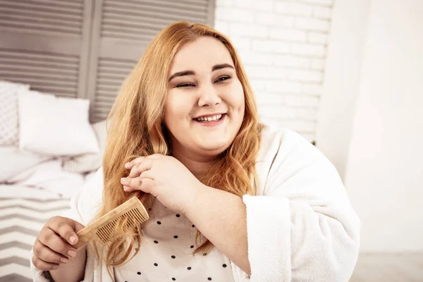 Beaming overweight lady with dismissed hair sitting in bedroom