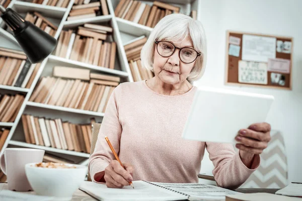 Concentrated blonde senior female person making notes — Stock Photo, Image
