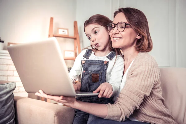 Deliziosa donna gioiosa che tiene un computer portatile davanti a sua figlia — Foto Stock