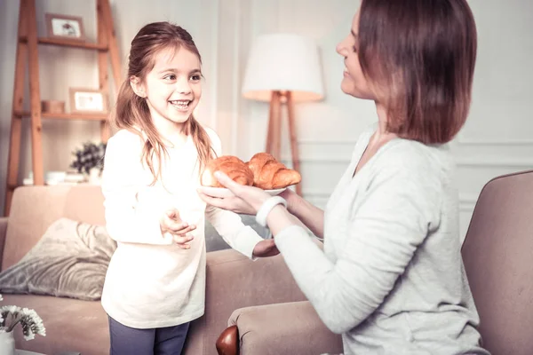 Delighted happy woman offering croissants to her daughter — Stock Photo, Image