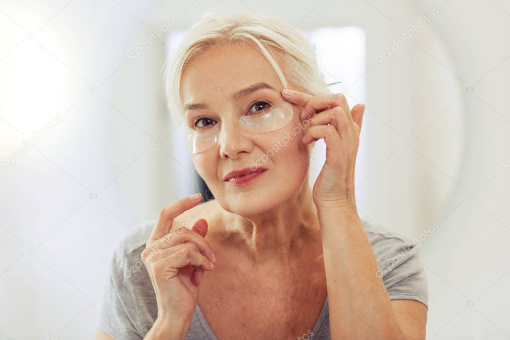 Positive joyful woman applying eye patches on the face