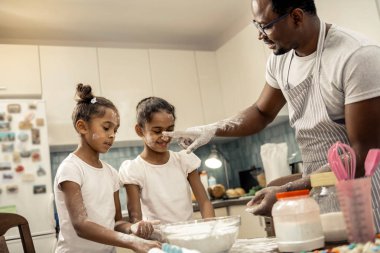 Baba kızlarını burun üzerinde biraz un koyarak çizgili önlük giyiyor