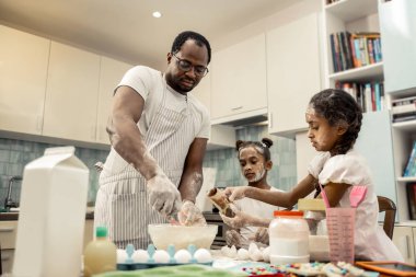 Two helpful funny daughters feeling involved in cooking with father