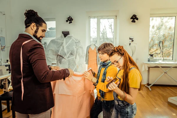 Сын помогает отцу держать светло-розовую ткань во время проектирования одежды — стоковое фото