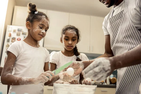 Dark-haired daughters with faces in flour helping father in kitchen — 图库照片