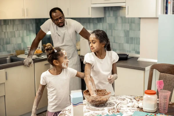父亲穿着条纹围裙看着他的女儿们做纸杯蛋糕 — 图库照片
