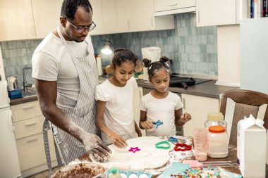 Two daughters feeling amazing while making cookies with father