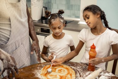 Pizza pişirme sırasında domates sosu yayılan iki yararlı kız