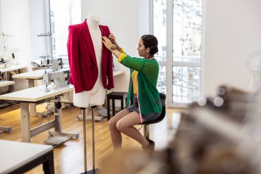 Genç Asyalı esmer terzi bir yeşil hırka ceket ile çalışma içinde