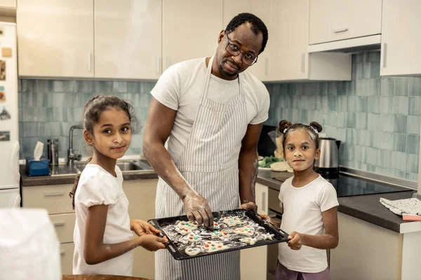 Daughters helping their father putting cookies into oven