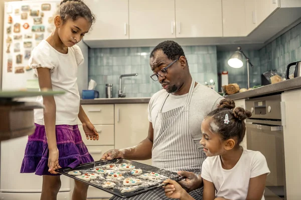 Friendly cheerful father and his girls looking at their cookies — Φωτογραφία Αρχείου