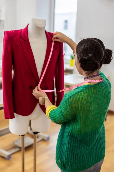 褐发女郎亚洲设计师在一个绿色开衫做测量 — 图库照片