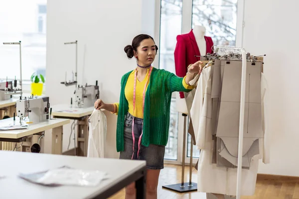 Jonge slanke Aziatische modeontwerper in een kort rokje, kijken naar de patronen voor kleding — Stockfoto