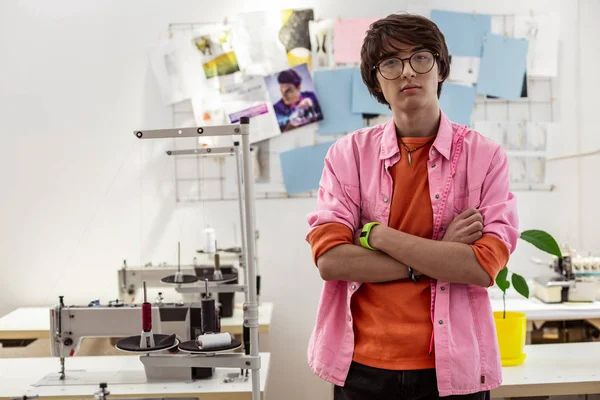 Young male asian stylist in a pink shirt standing near sewing machines