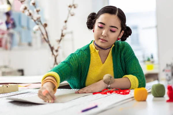 Cute brunette asian dressmaker with pink eyeshadows looking focused