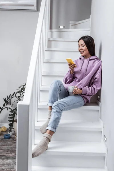 Slim ελκυστική γυναίκα που φοράει τζιν και μωβ hoodie κάθομαι στις σκάλες — Φωτογραφία Αρχείου