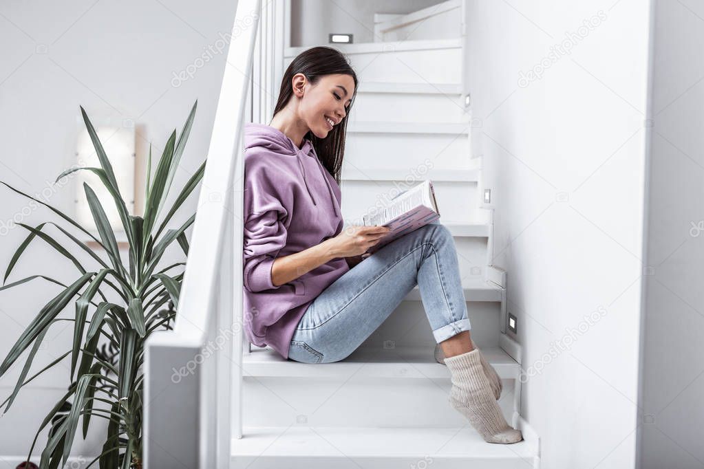 Woman with book. Woman wearing jeans and warm socks reading book sitting on stairs at her home