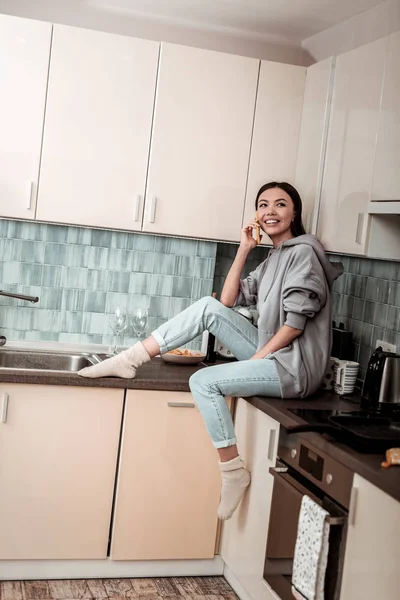 Темноволосая женщина в джинсах и теплых носках сидит на кухне — стоковое фото