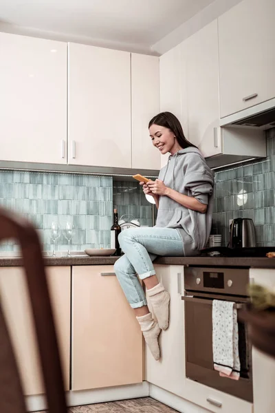 Μελαχρινός γυναίκα που φοράει τζιν και υπερμεγέθη hoodie κάθεται στην κουζίνα — Φωτογραφία Αρχείου