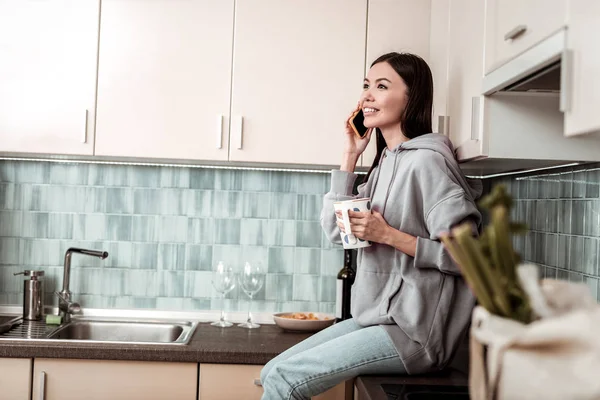 Mujer de cabello oscuro con sudadera con capucha de gran tamaño sentado cerca del fregadero — Foto de Stock