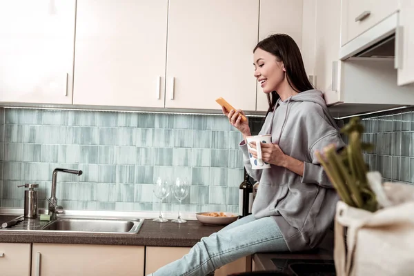 Mujer feliz descansando en la cocina usando las redes sociales —  Fotos de Stock