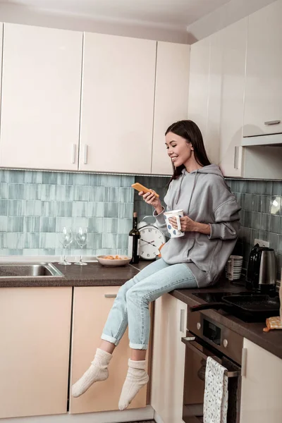 Veselá žena sedí mezi vařič a dřez čtení novinek — Stock fotografie