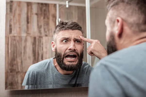 Young man feeling overemotional seeing acne on his face — Stock Photo, Image