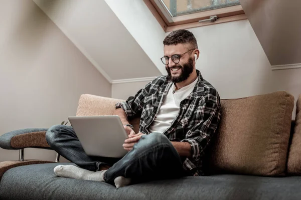 Веселий щасливий чоловік сидить на дивані зі своїм ноутбуком — стокове фото